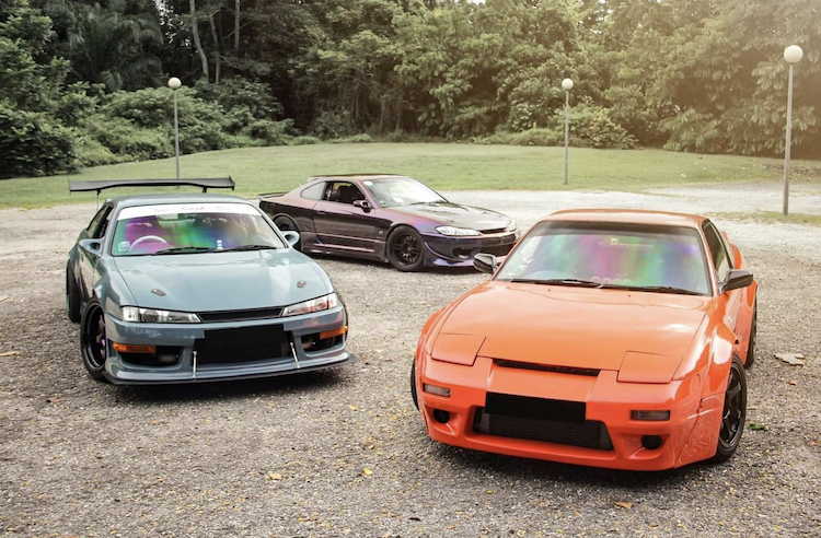 Three colorful cars parked in a lot, showcasing a variety of styles and designs, highlighting JDM car appeal